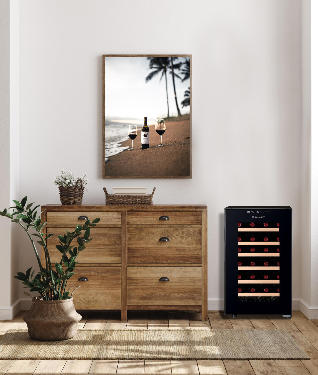 Ein Raum mit einem gerahmten Bild von Wein am Strand. Ein Holzschrank, ein Weinkühler und eine Topfpflanze sind ebenfalls vorhanden.