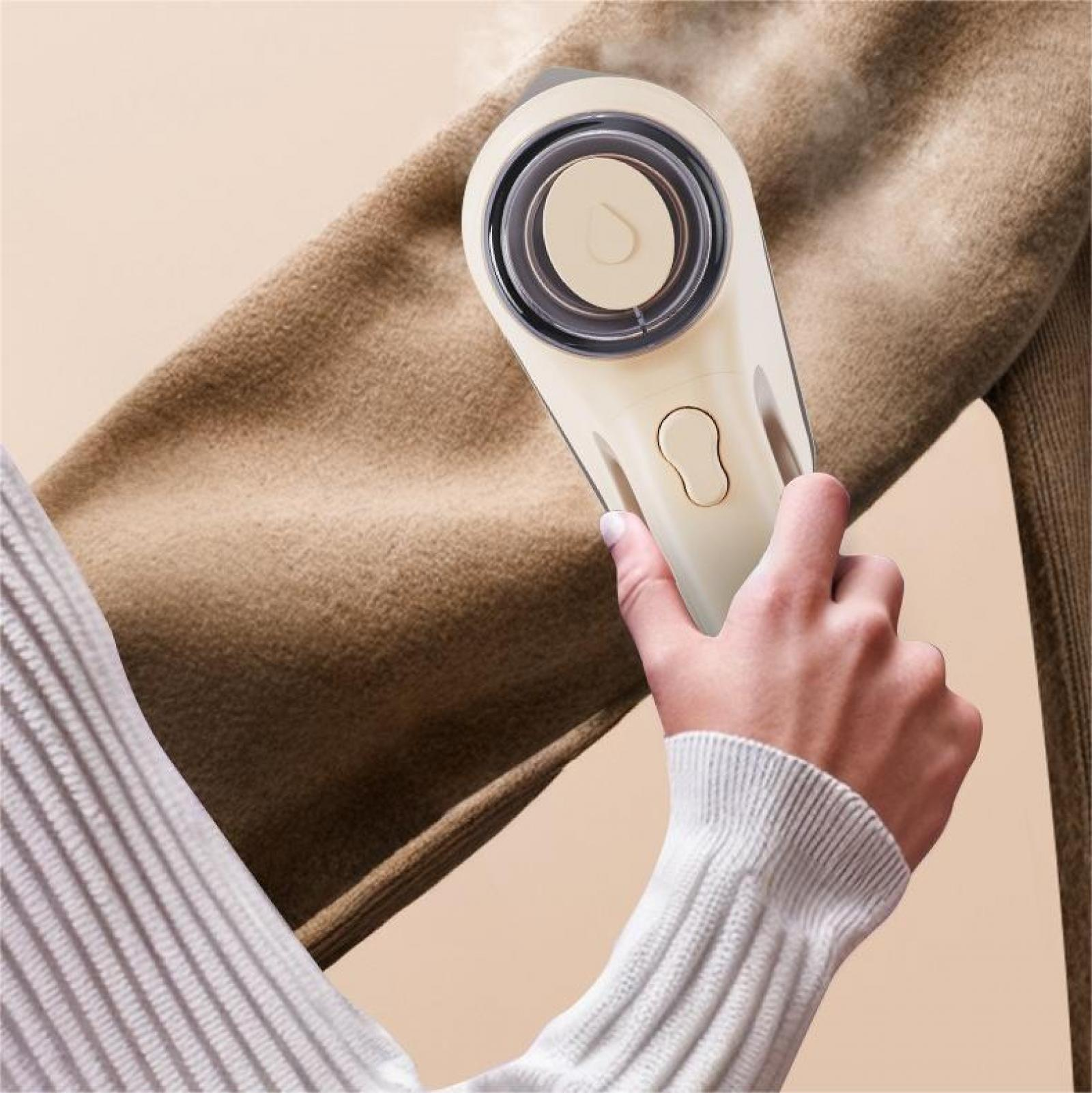 Eine Hand hält einen Stoffrasierer über einem braunen Pullover. Der Rasierer ist beige, und der Pullover wird gereinigt.