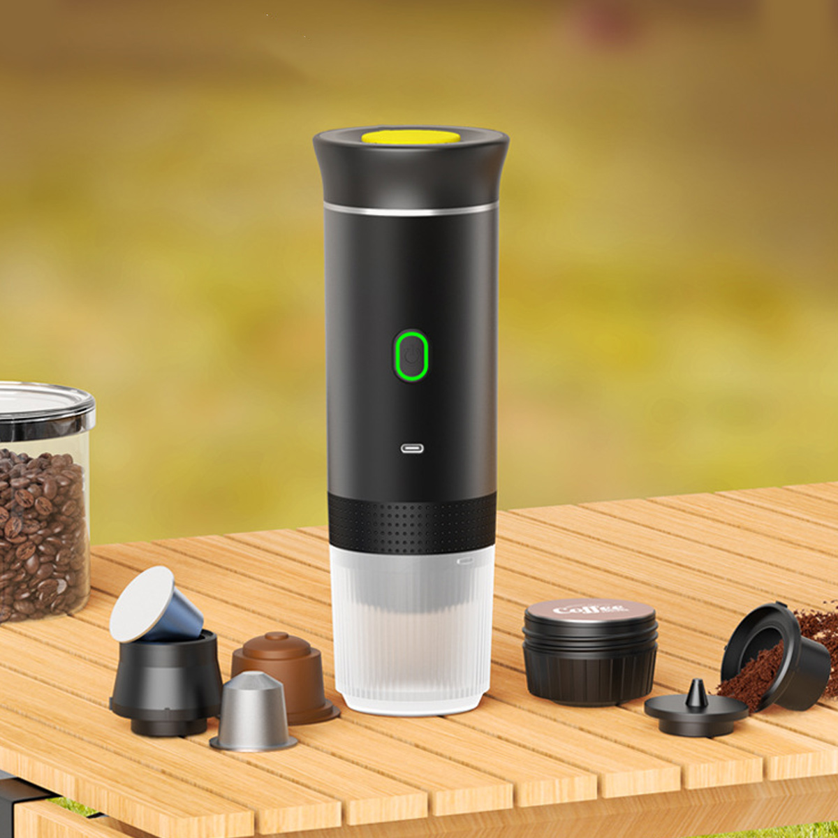 Ein schwarzer Kaffeezubereiter mit gelbem Deckel und grünem Einschaltknopf. Kaffeepads und Bohnen liegen daneben auf einem Holztisch.