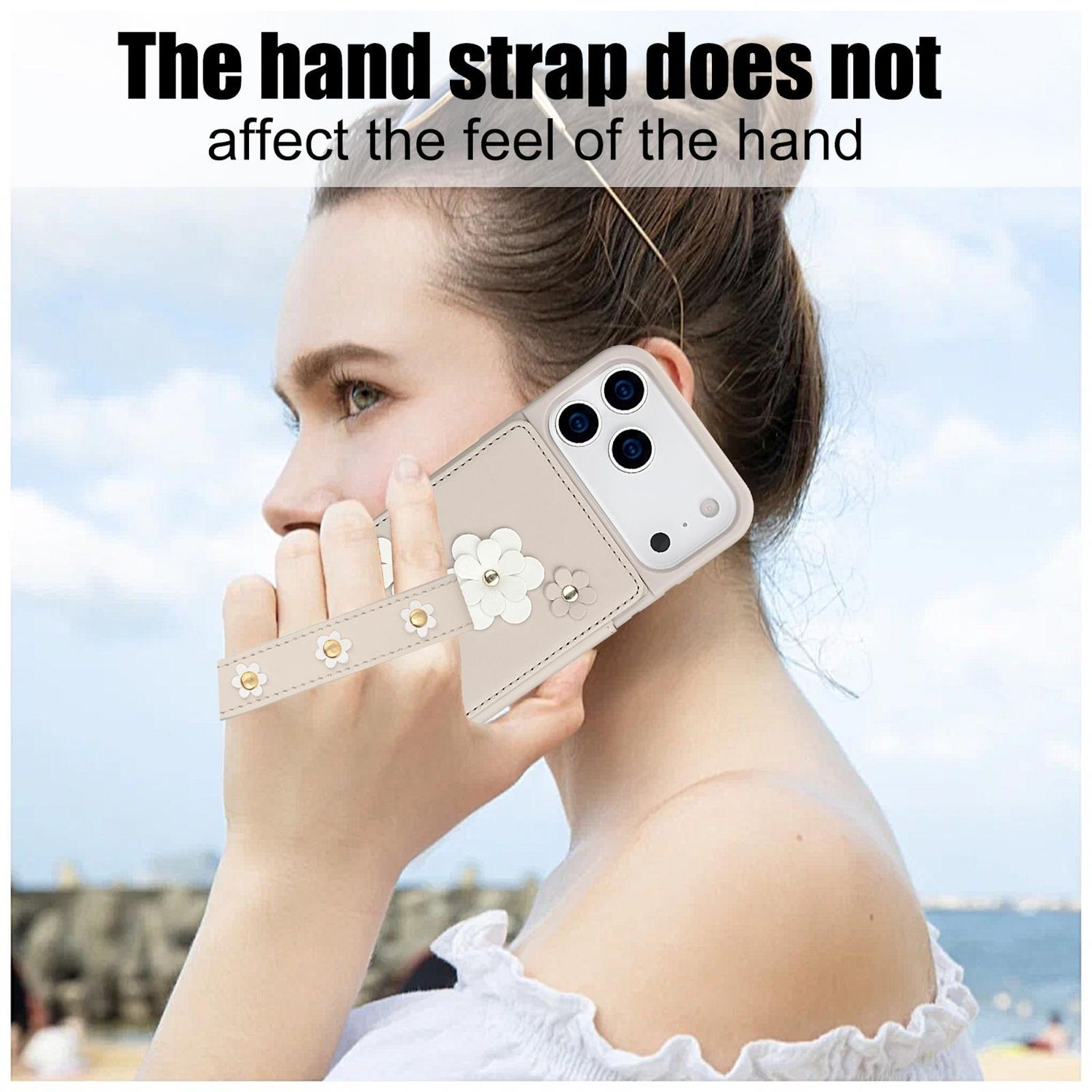 Una mujer sostiene un teléfono con una correa floral para la mano. El teléfono está en una funda beige. El fondo es una escena de playa borrosa.