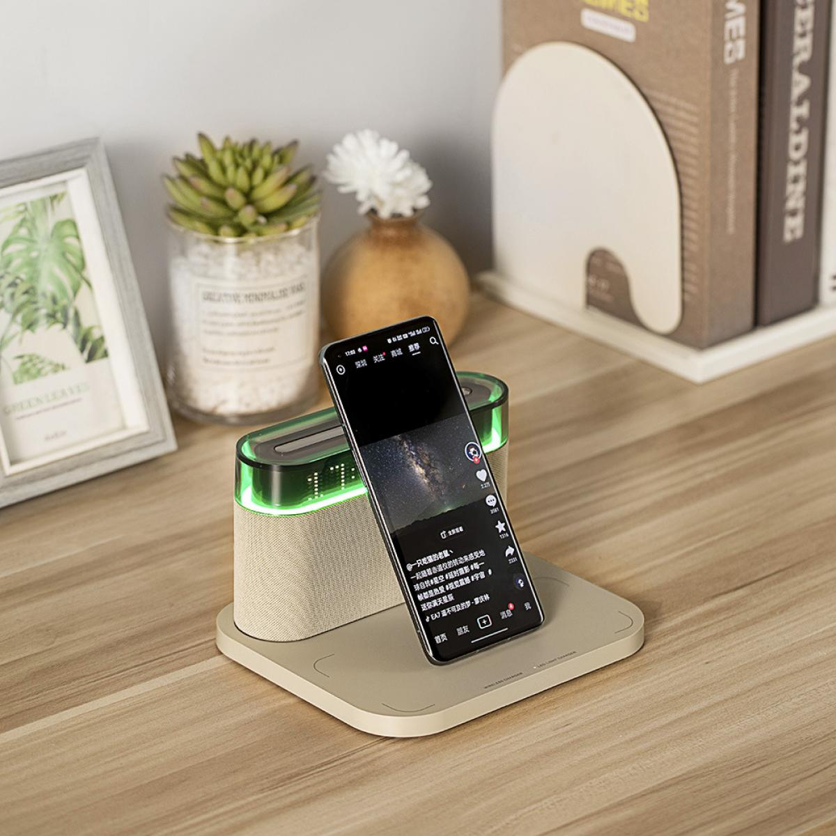 Ein Telefon zeigt ein Video und liegt auf einer Ladestation. Eine Sukkulente, eine Vase mit weißer Blume und Bücher sind ebenfalls im Bild.