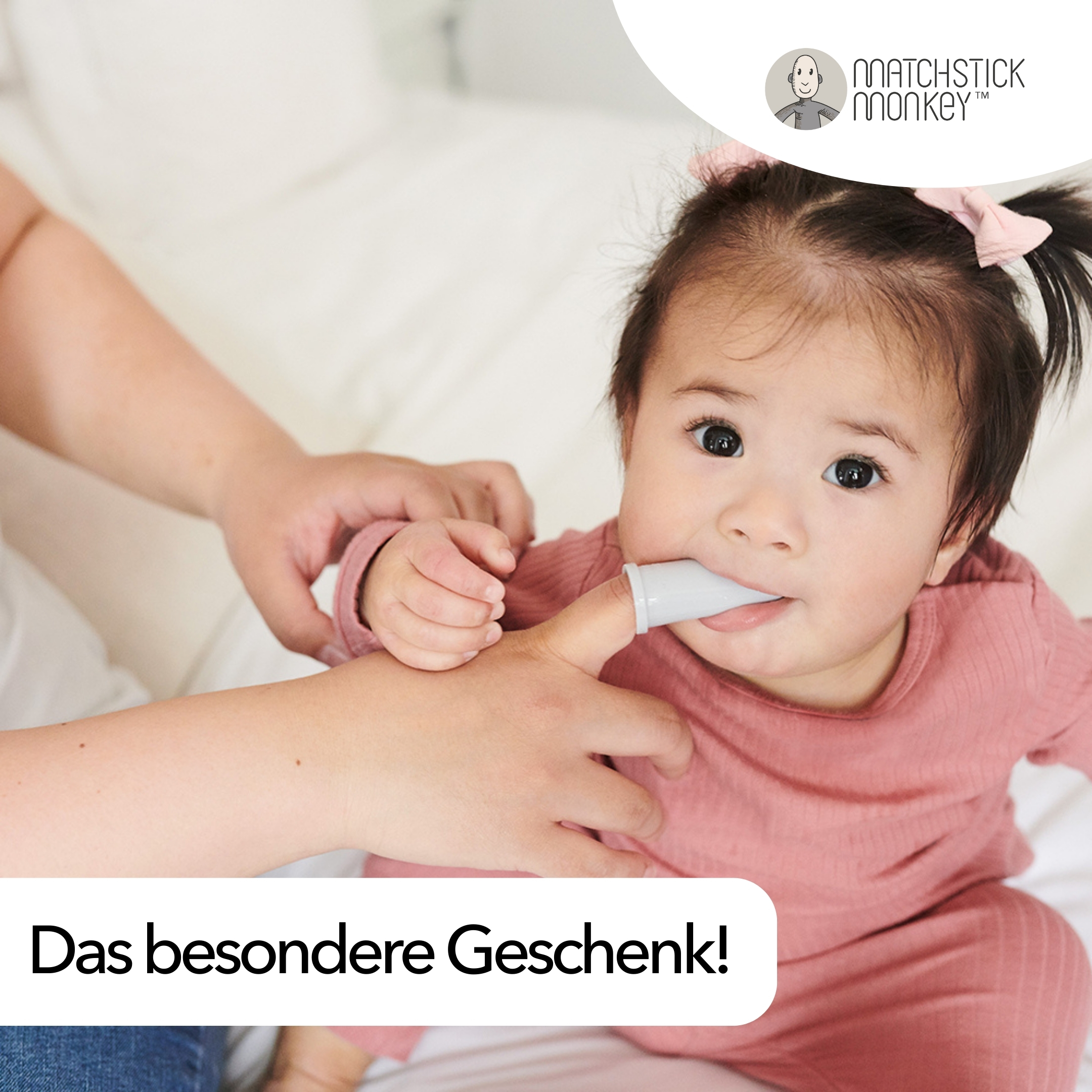 Ein Baby in rosa Kleidung, eine Fingerbürste im Mund und eine Hand, die sie hält. Text: Das besondere Geschenk!