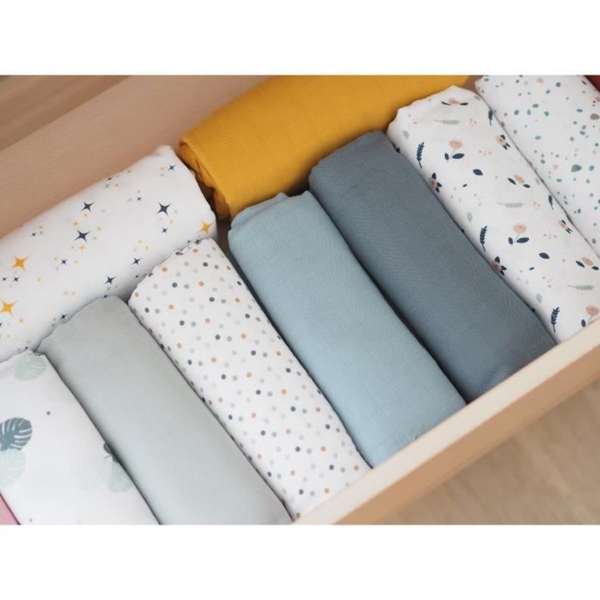 Holzschublade gefüllt mit zusammengerollten Babydecken. Farben sind Gelb, Blau, Grau und Weiß mit Stern- und Punktdesign.