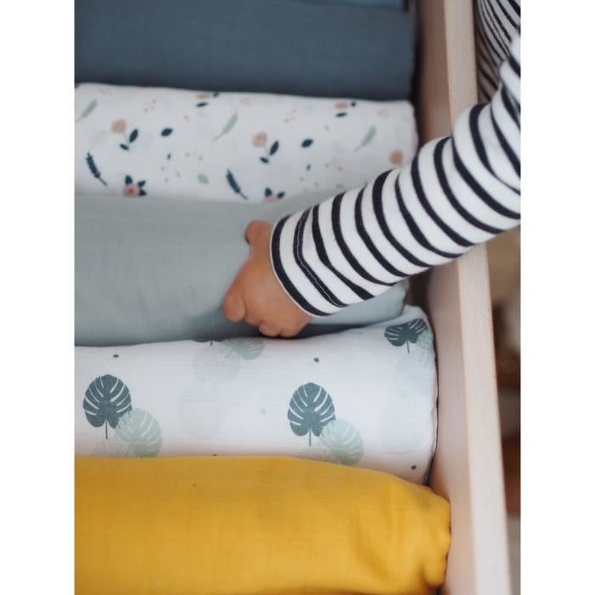 Ein Kinderarm in gestreiftem Hemd greift nach einer gerollten Decke in einer Schublade. Verschiedene gerollte Decken in verschiedenen Farben sind sichtbar.
