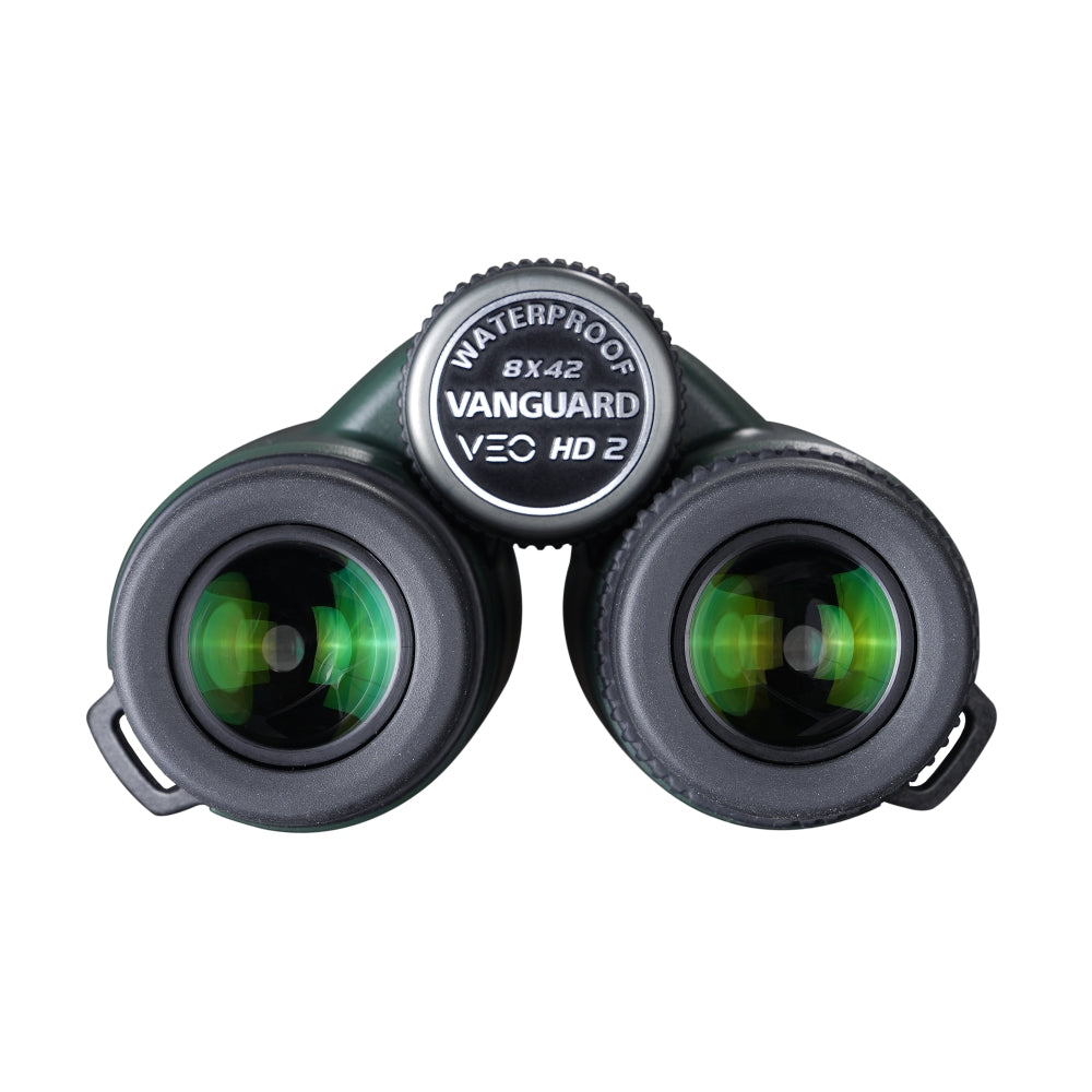 Primer plano de binoculares negros y verdes con la palabra 'WATERPROOF' y 'VANGUARD'. Las lentes reflejan luz verde.