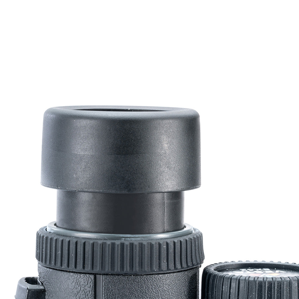 Primer plano de un monocular negro con tapa protectora. El anillo de enfoque es visible, y una tapa de lente está en la parte inferior derecha.