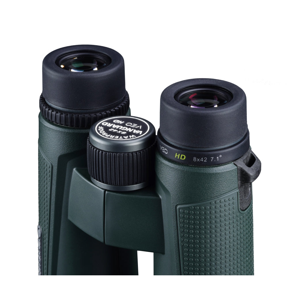 Primer plano de binoculares verdes con copas oculares de goma negra. La rueda de enfoque central tiene texto. Los binoculares están sobre fondo blanco.