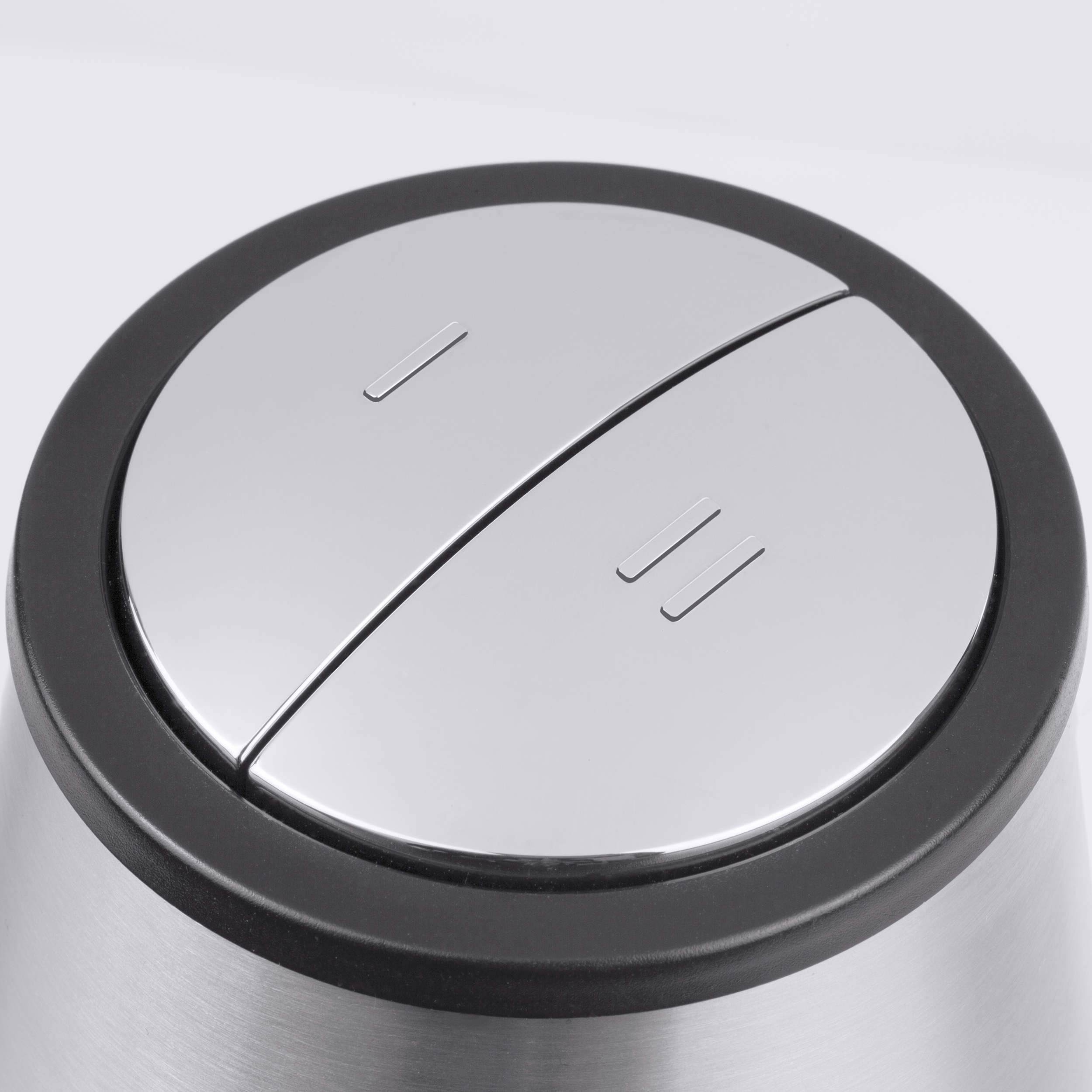 Primo piano di un pulsante metallico argentato con due sezioni. Un anello nero lo circonda. Due piccole linee sono visibili.