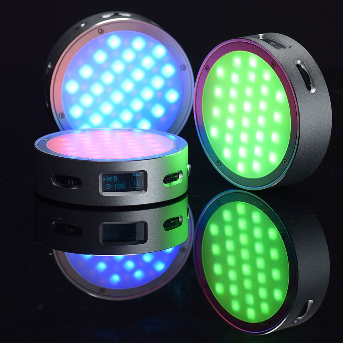 Drei LED-Leuchten in verschiedenen Farben: Blau, Grün und Rosa. Sie spiegeln sich auf einer schwarzen, glänzenden Oberfläche. Jede hat ein Display.
