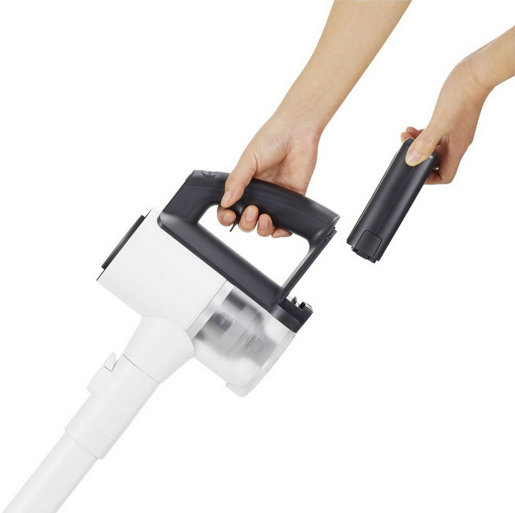 Le mani assemblano un aspirapolvere senza fili bianco e nero con una batteria separata.