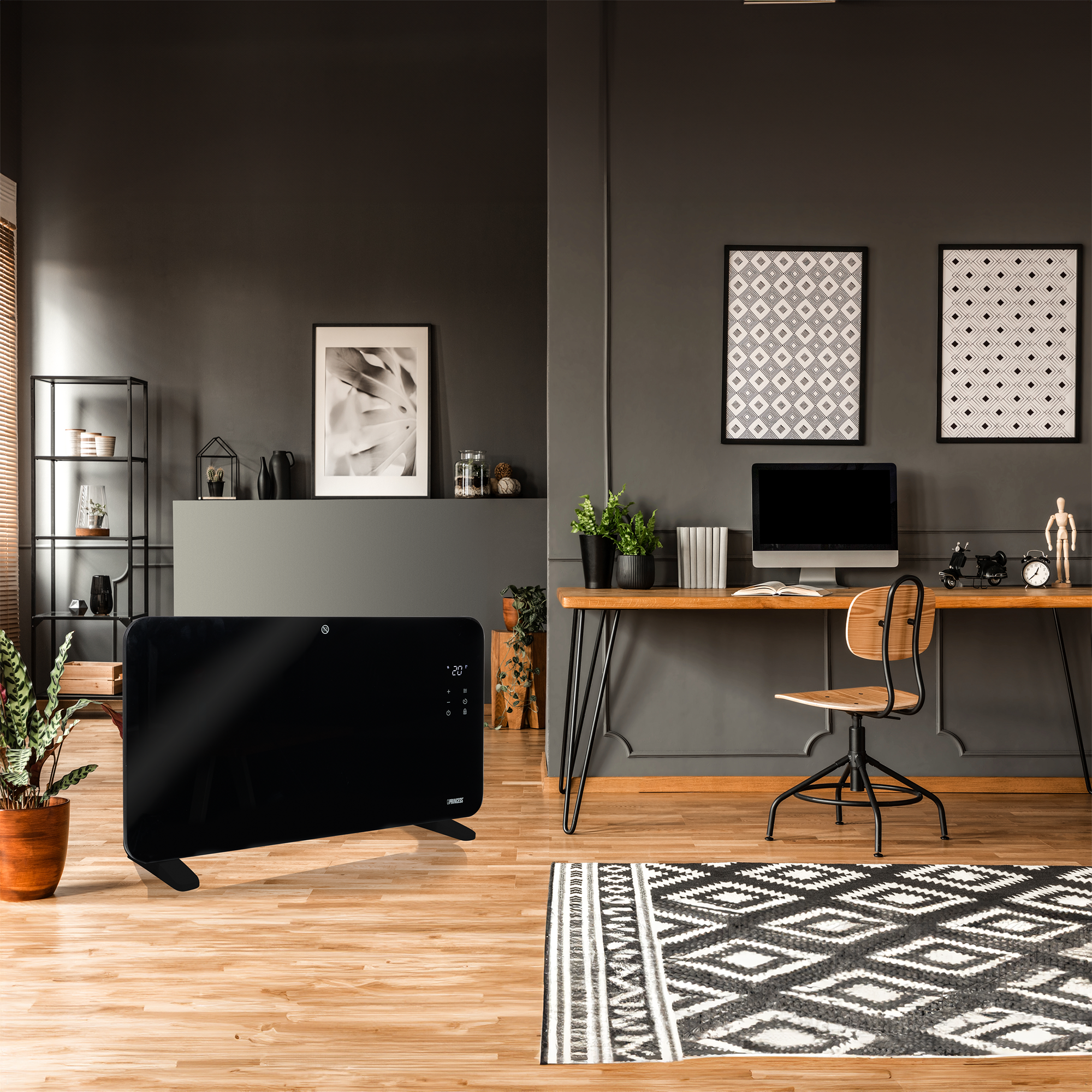 Een moderne kamer met een zwarte kachel, bureau met computer en een patroonkleed. Planten en kunstwerken sieren de muren.