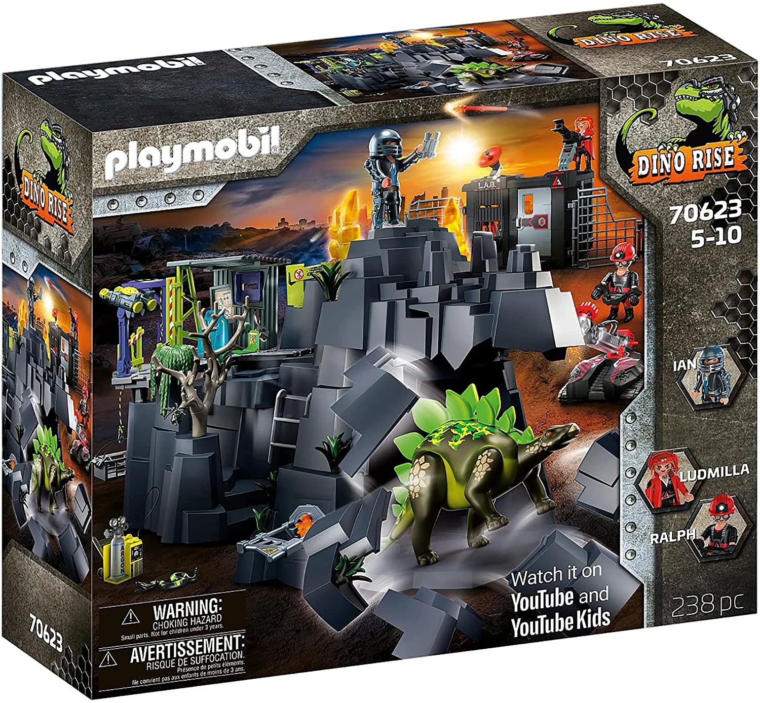 Playmobil Dino Rise Set-Box. Enthält einen Dinosaurier, Figuren, ein Labor und felsiges Gelände. Auf der Box steht „Watch it on YouTube“.
