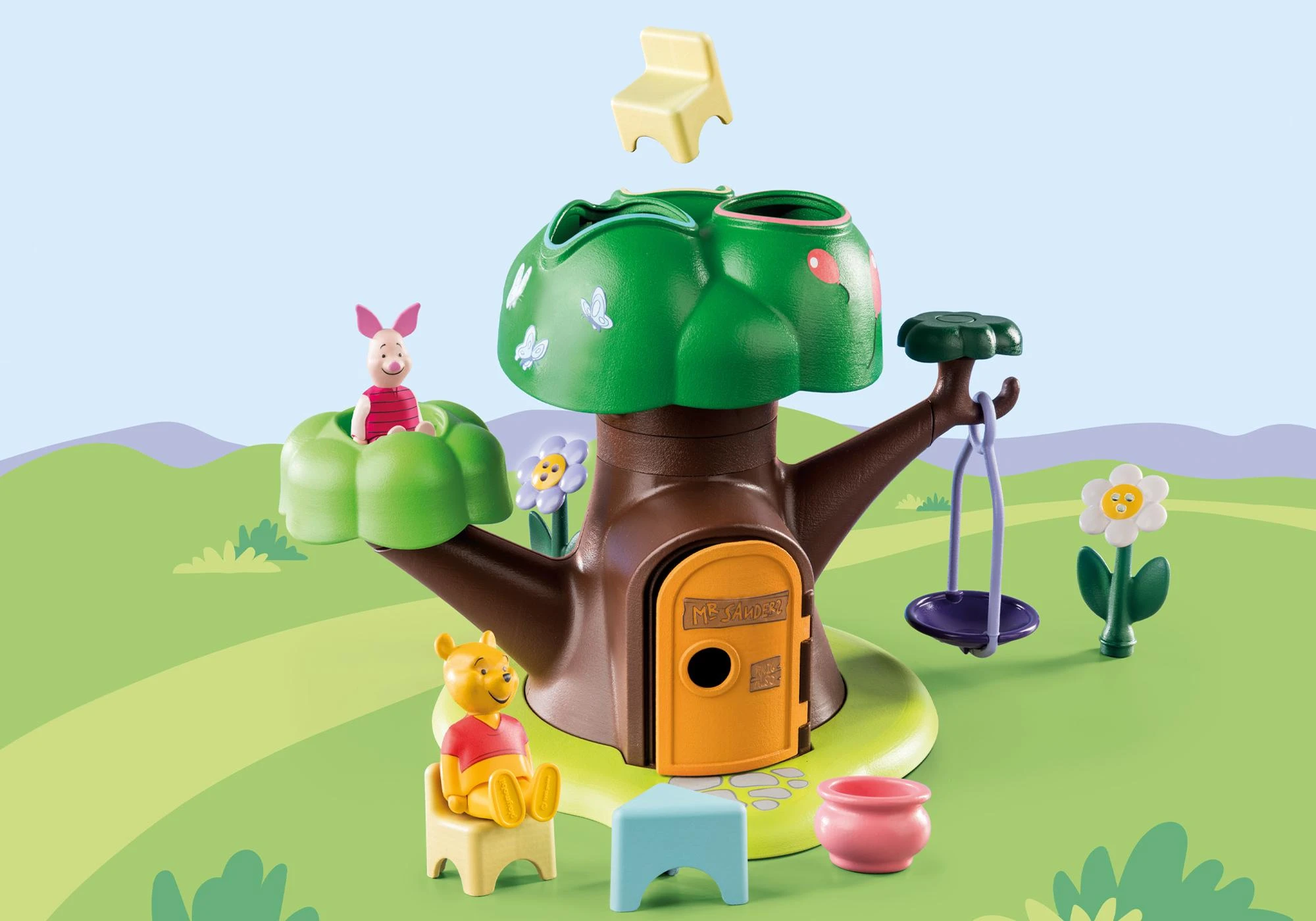 Eine Baumhausszene mit Winnie-the-Pooh-Figuren. Ferkel sitzt auf einem grünen Busch, und Puuh sitzt auf einem Stuhl. Eine Schaukel und eine Blume sind sichtbar.