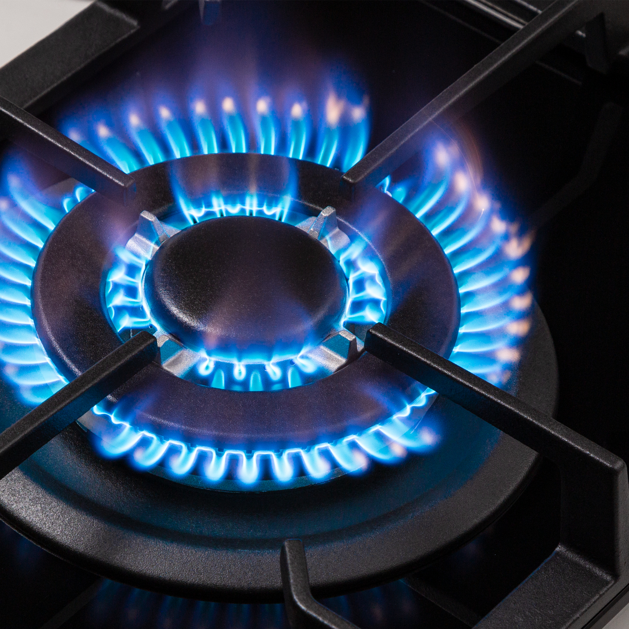 Primo piano di un bruciatore di fornello a gas con fiamme blu brillante. Griglie nere circondano le fiamme, su una superficie scura.