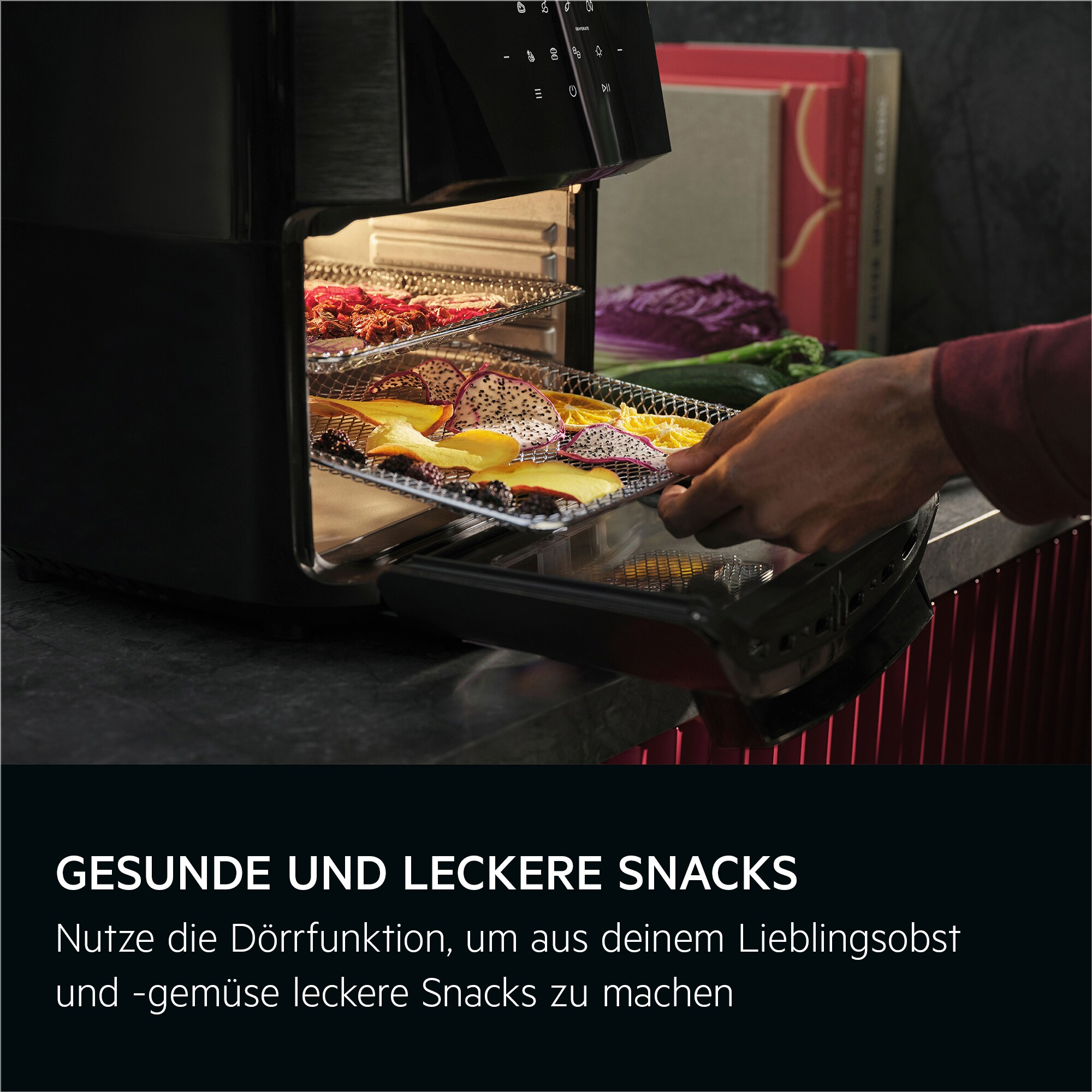 Ein Luftfritteuse mit Trocknungsfunktion, gefüllt mit geschnittenem Obst und Gemüse. Hand öffnet die Friteuse. Der Hintergrund ist verschwommen.