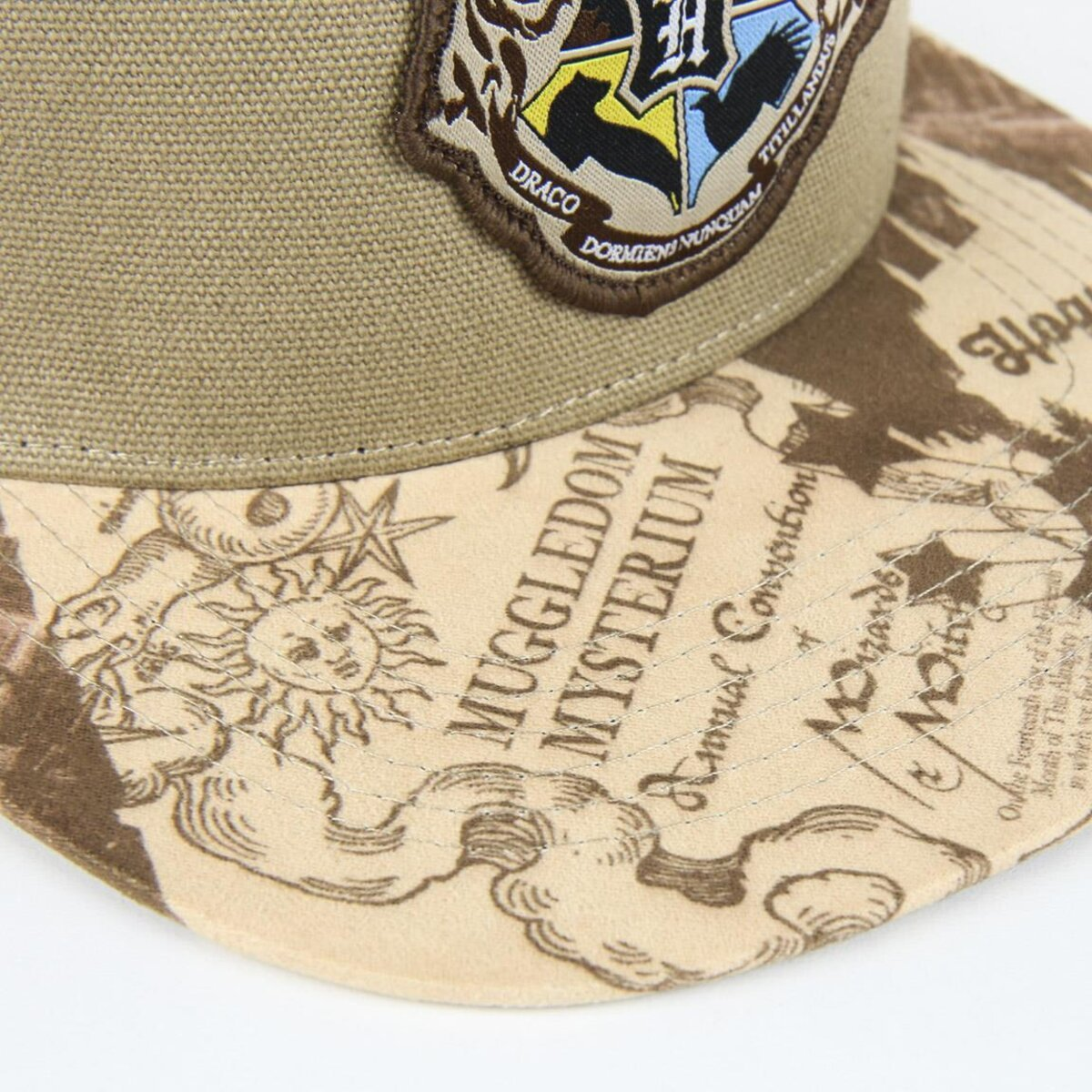 Una gorra color canela con un parche del escudo de Hogwarts. La visera presenta ilustraciones y texto relacionados con 'Muggledom Mysterium' y 'Annual Convention'.