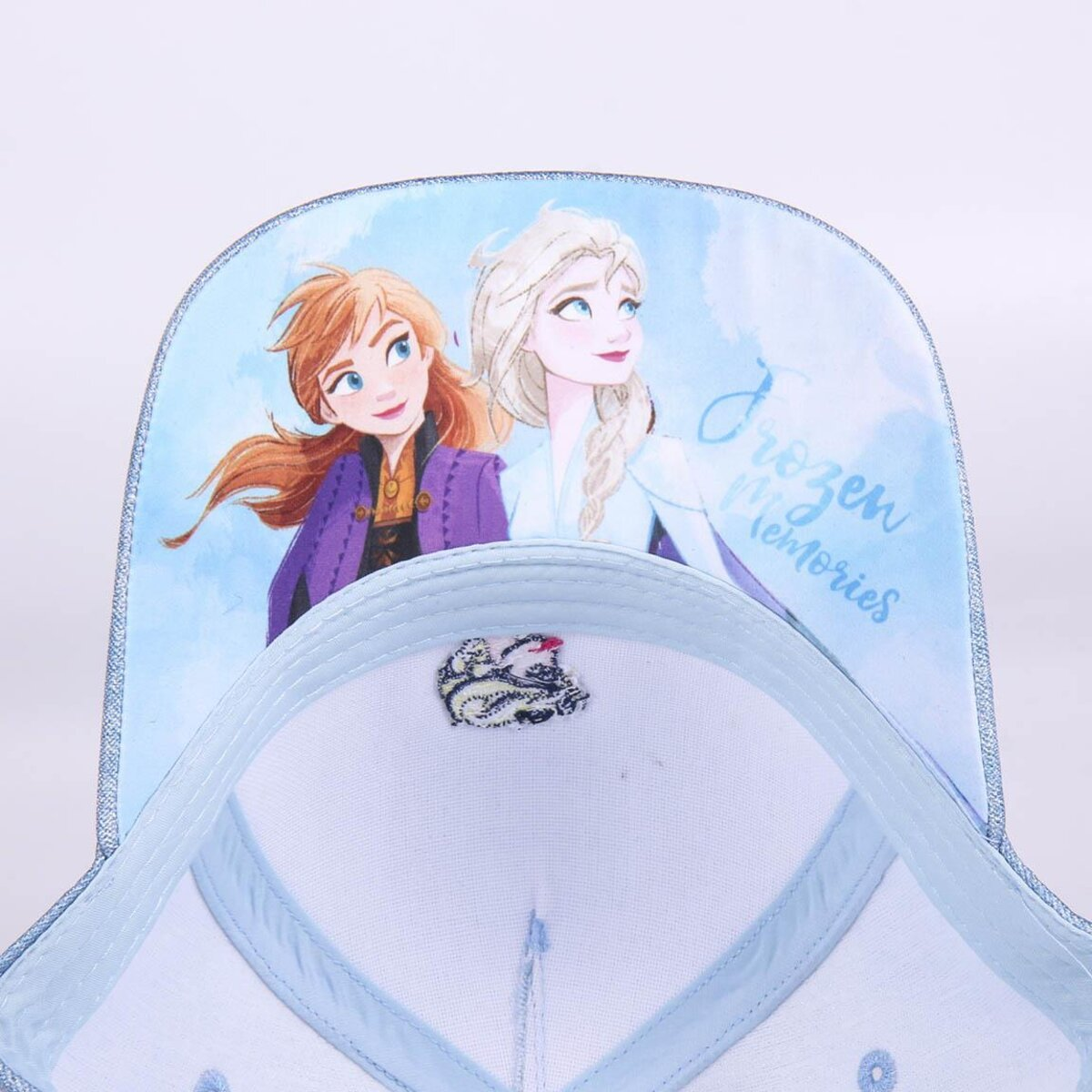 Una gorra con Anna y Elsa de Frozen, con texto 'Frozen Memories'. La gorra es azul claro con interior blanco y un pequeño parche bordado.