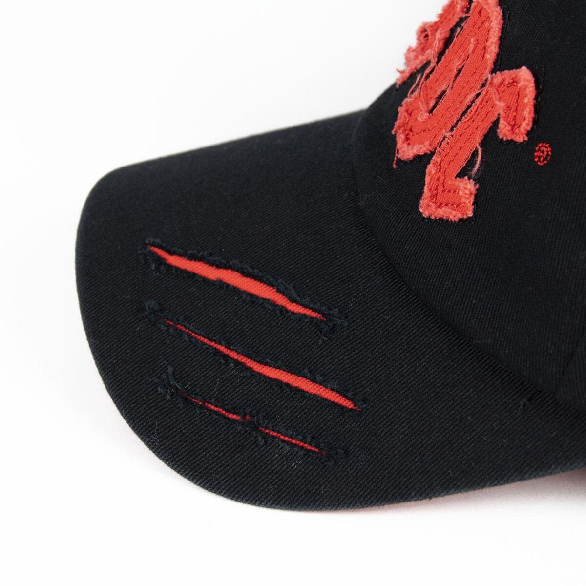 Una gorra negra con diseño bordado en rojo y detalles desgastados. Cuenta con tres cortes rojos en la visera y un logotipo rojo.