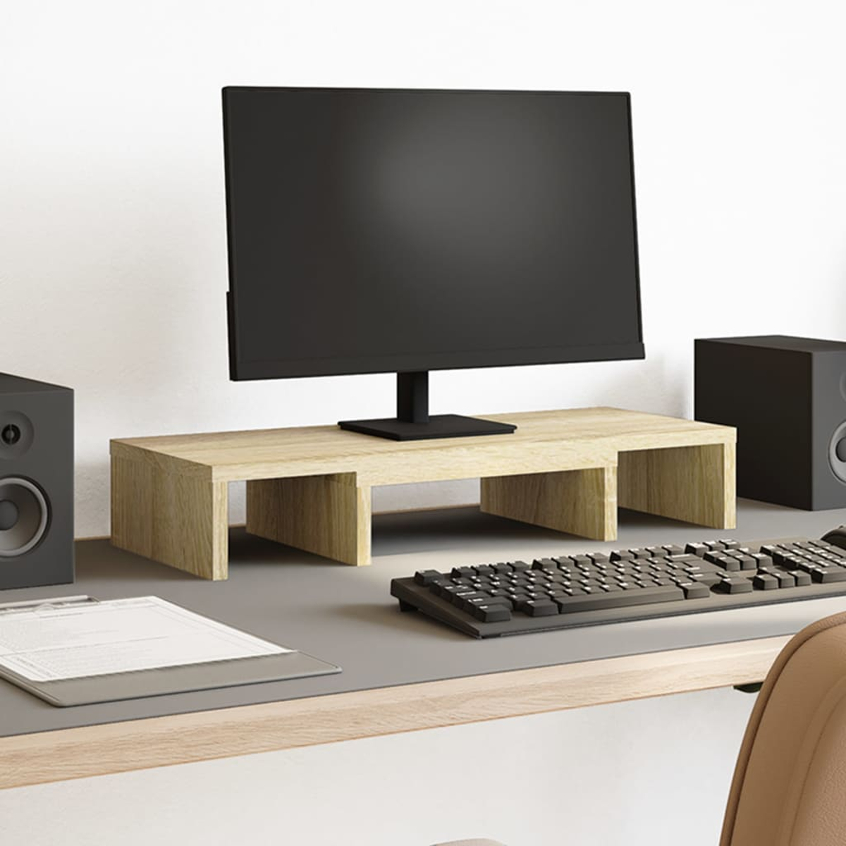 Ein Computer-Setup mit einem Monitor auf einem Holzständer. Auf dem Schreibtisch befinden sich eine Tastatur, Lautsprecher und eine Klemmmappe. Ein Stuhl ist sichtbar.