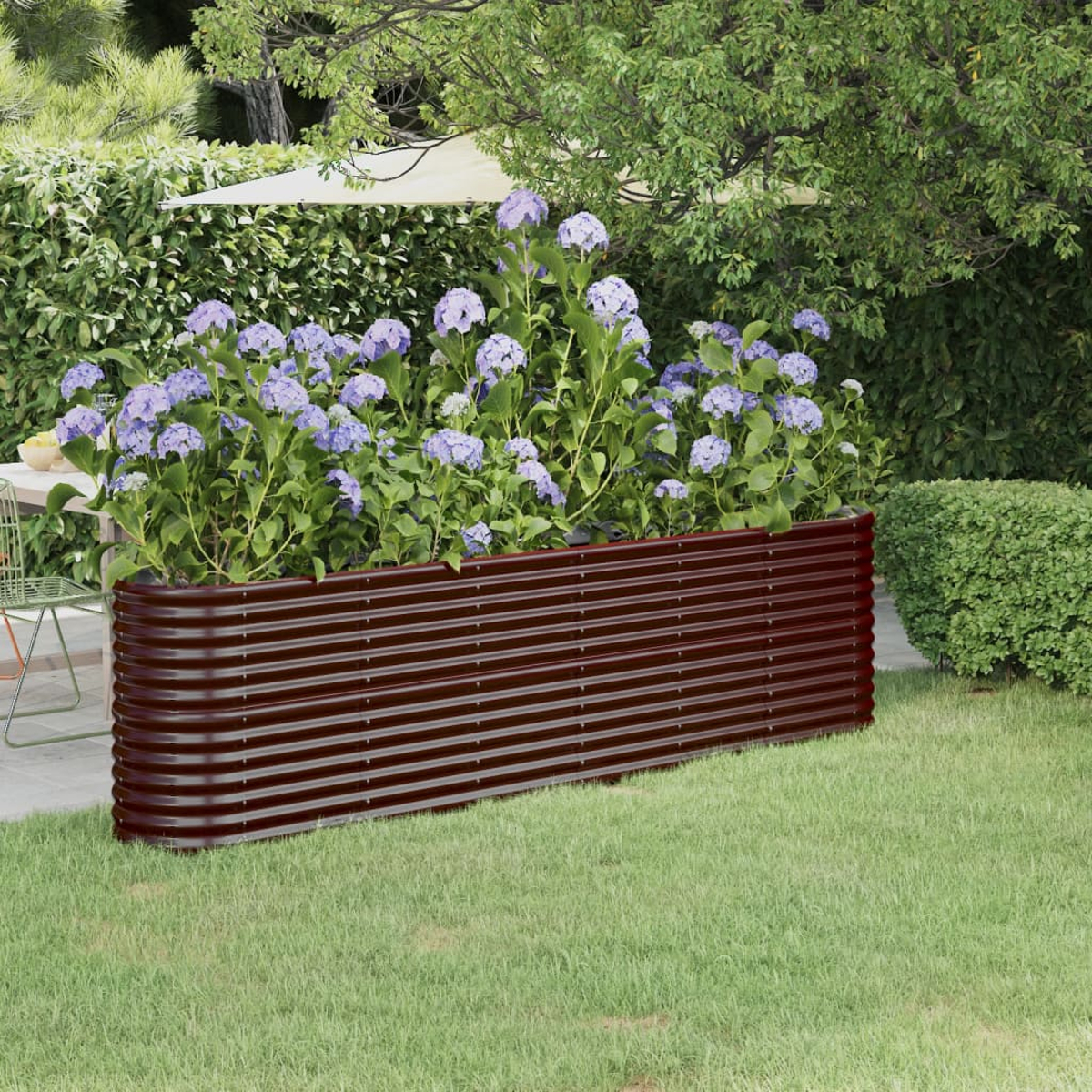 Ein erhöhtes Blumenbeet mit lila Blumen befindet sich in einem grünen Garten. Ein braunes Metallbett hält die Blumen. Bäume und eine Hecke sind im Hintergrund.
