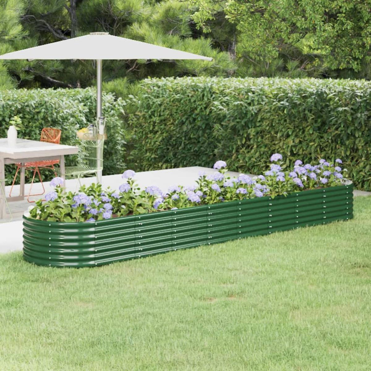 Eine Gartenszene mit einem grünen Metallpflanzer, gefüllt mit lila Blumen. Es gibt einen weißen Sonnenschirm, Tisch, Stühle und grüne Hecke.