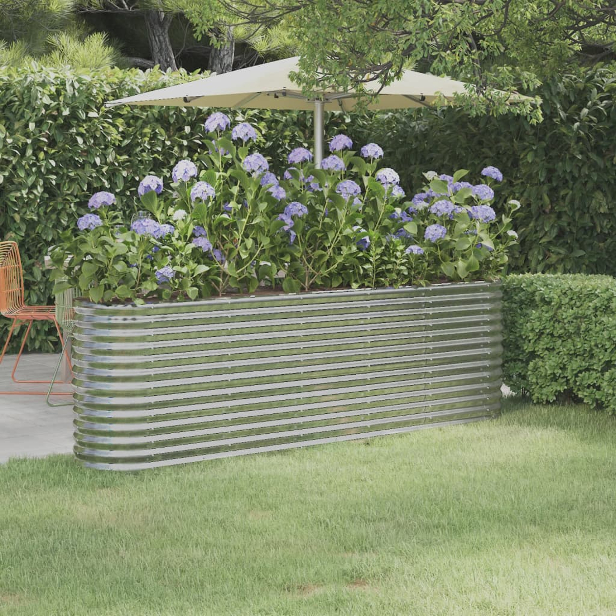 Ein metallenes Hochbeet mit blauen Blumen steht auf Gras. Ein Schirm und Bäume sind im Hintergrund. Ein Stuhl auf einer Terrasse ist zu sehen.