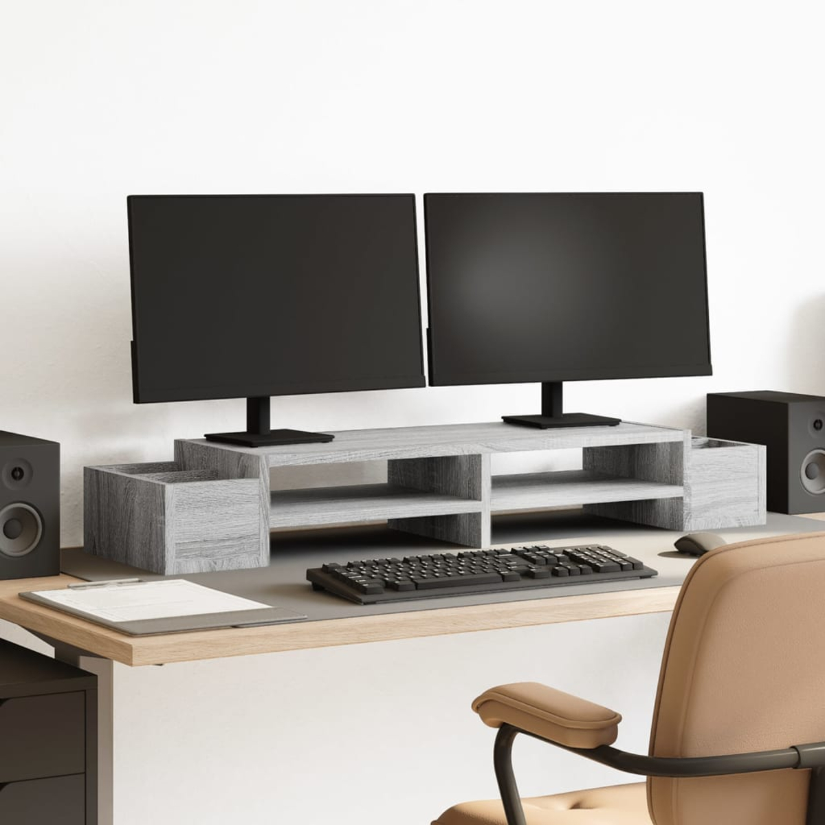 Ein Schreibtisch mit zwei Monitoren auf einem Ständer, Tastatur, Maus, Lautsprechern und einem Stuhl. Der Schreibtisch ist helles Holz, der Hintergrund ist weiß.