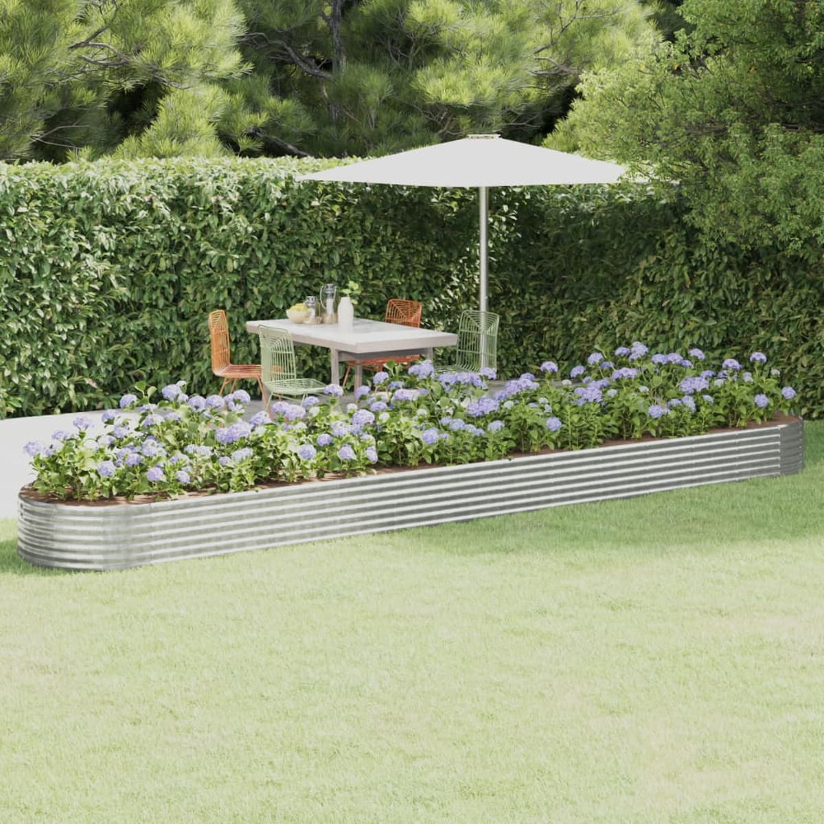 Eine Gartenszene mit Tisch, Stühlen und Schirm. Blumen in einem Metallpflanzer im Vordergrund. Grüne Hecke im Hintergrund.