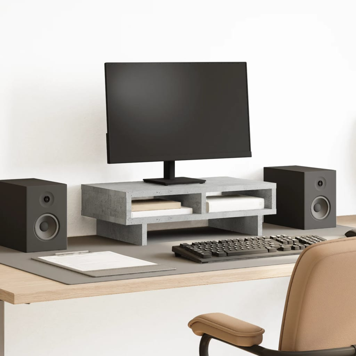 Ein Schreibtisch-Setup mit Monitor, Lautsprechern, Tastatur und Stuhl. Der Monitor steht auf einem Betonregal. Auf dem Schreibtisch liegt ein Notizblock.
