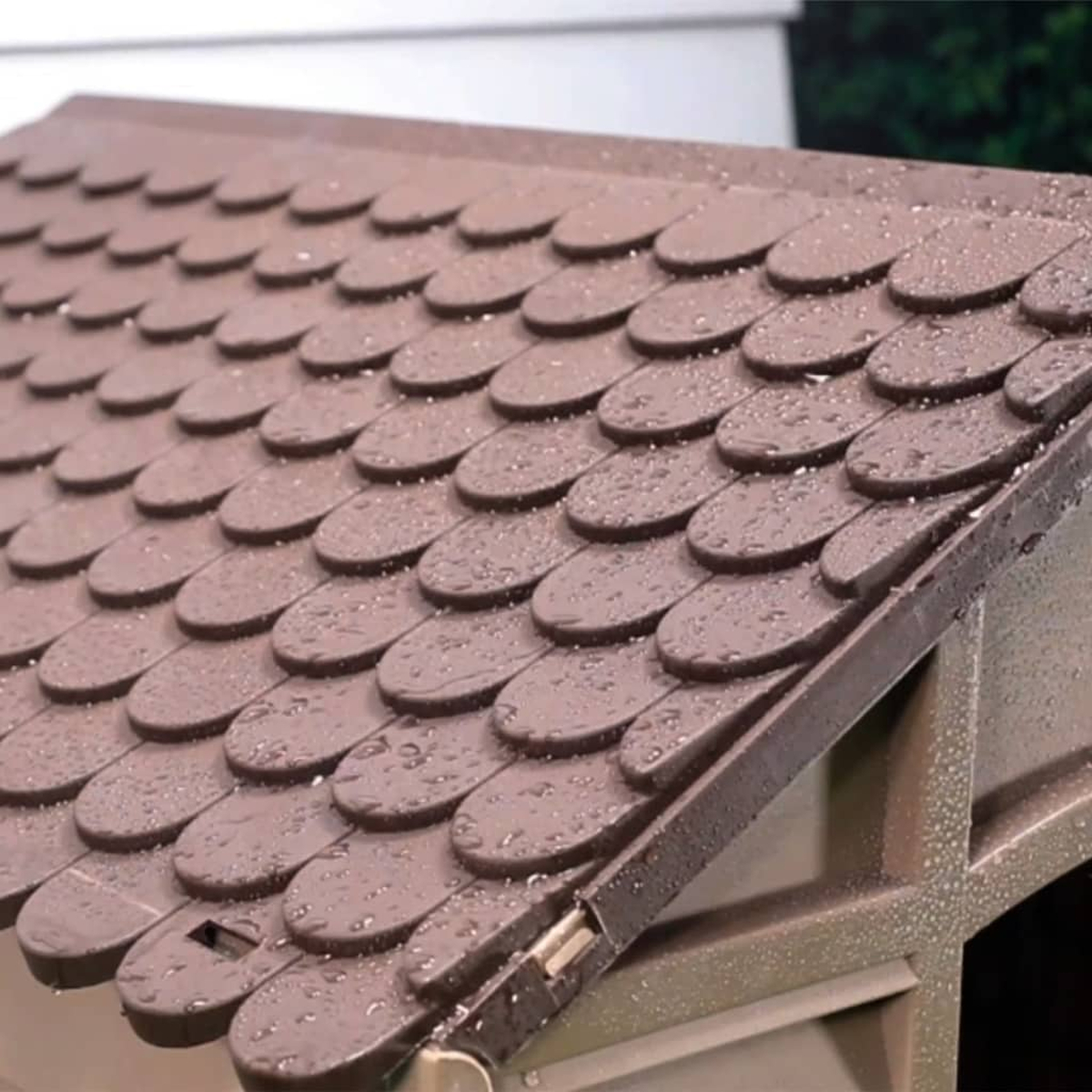 Nahaufnahme eines braunen Daches mit Wassertropfen. Das Dach hat ein sich überlappendes Schindelmuster. Braune Rahmen sind sichtbar.