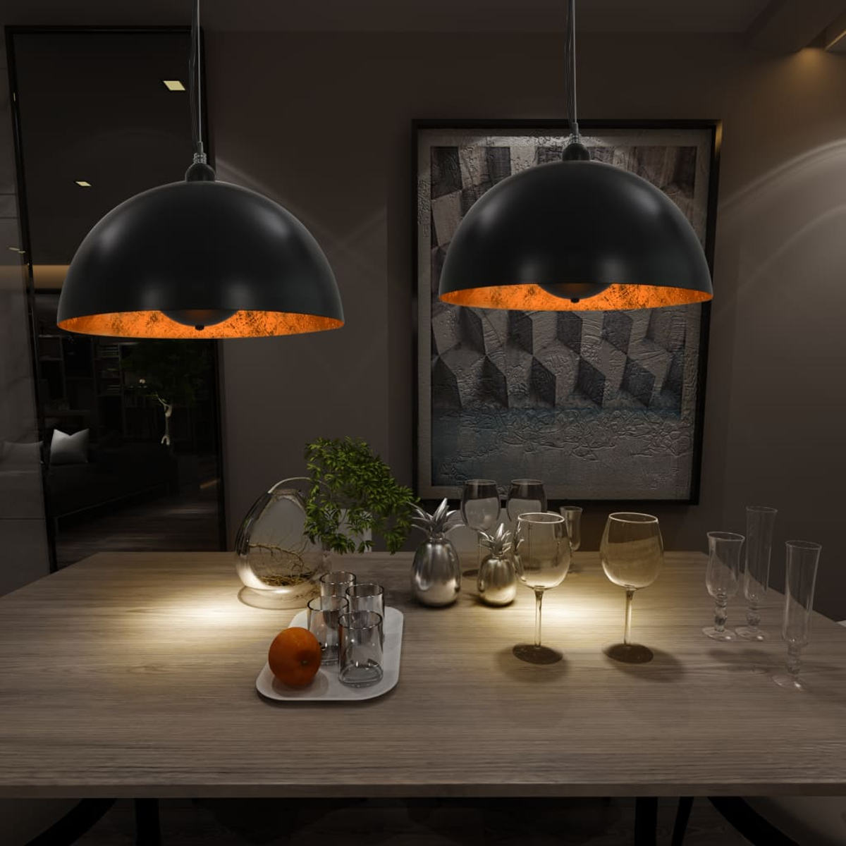 Zwei schwarze Lampen hängen über einem Holzesstisch mit Gläsern, Obst und Dekorationen. Im Hintergrund befinden sich ein Spiegel und Kunstwerke.
