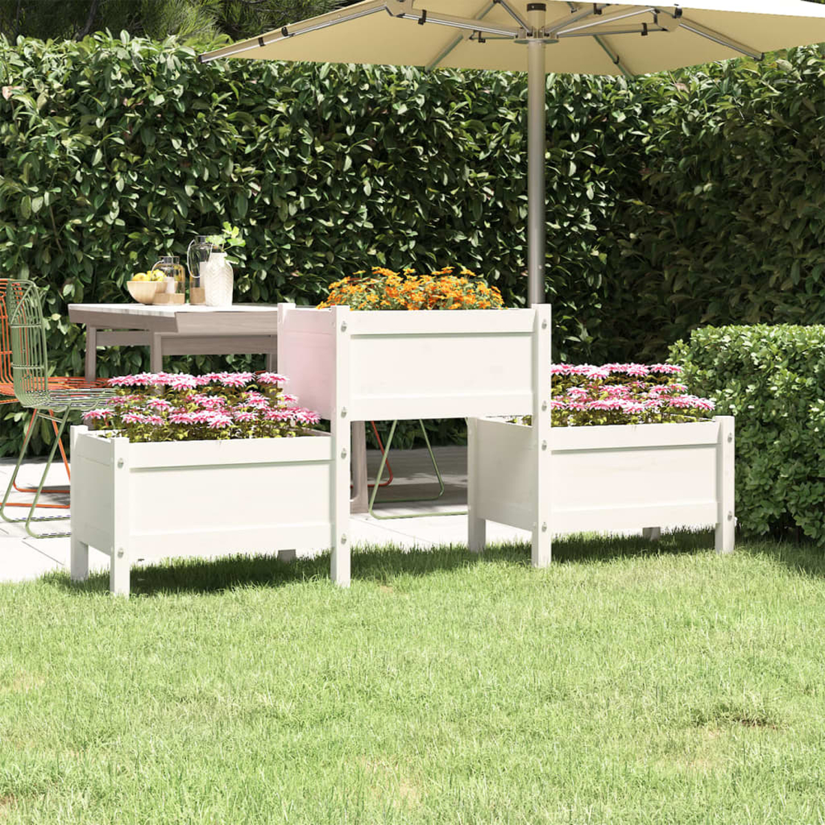 Szene im Freien mit weißen Pflanzgefäßen, gefüllt mit rosa und orangefarbenen Blumen. Ein Tisch, Stühle und ein Sonnenschirm befinden sich im Hintergrund, umgeben von Grün.
