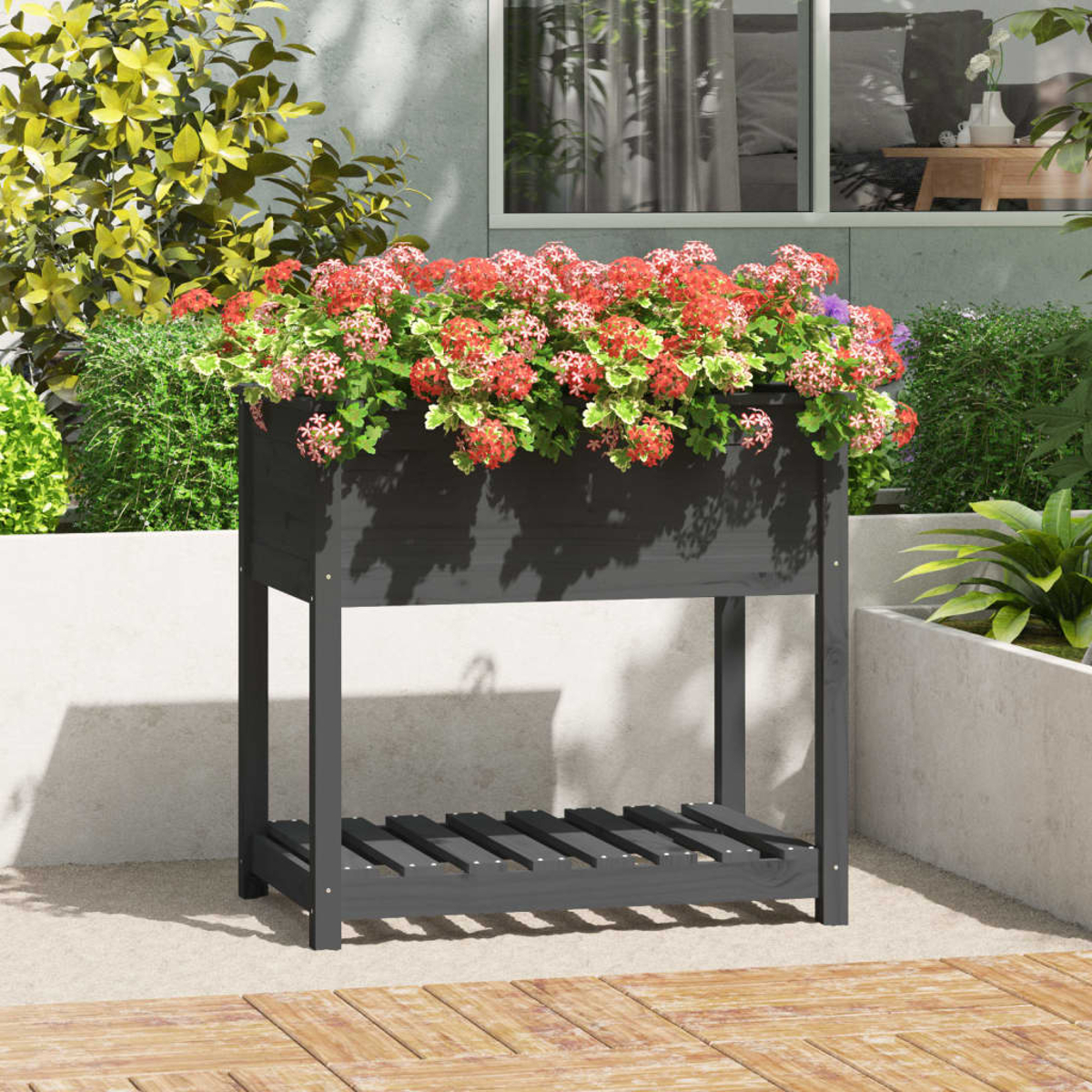 Ein dunkelgrauer Pflanzkasten mit roten Blumen. Er steht auf einer Terrasse mit Fenster und Grün im Hintergrund.