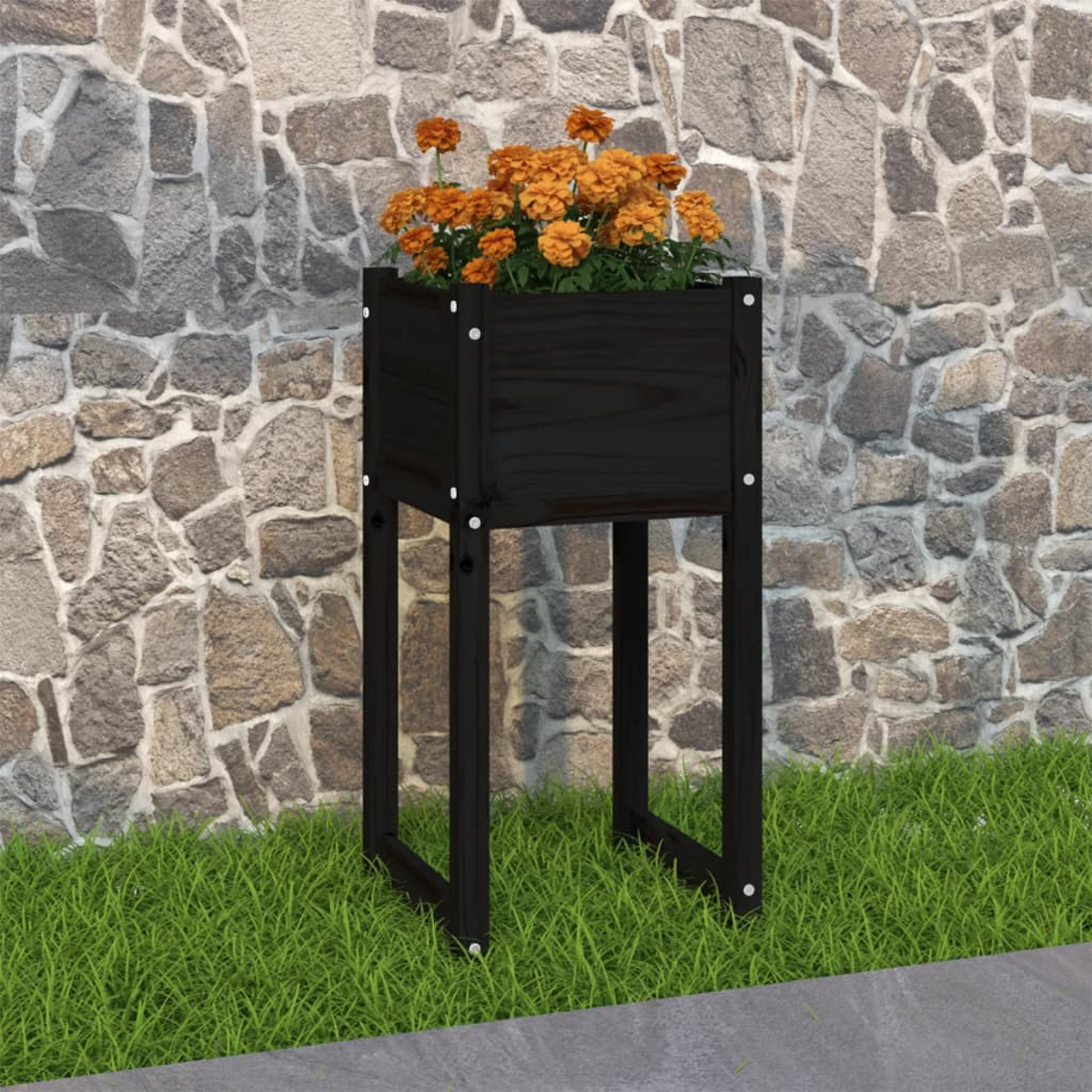 Ein schwarzer Holzpflanzer mit orangen Blumen steht auf Gras vor einer Steinmauer.