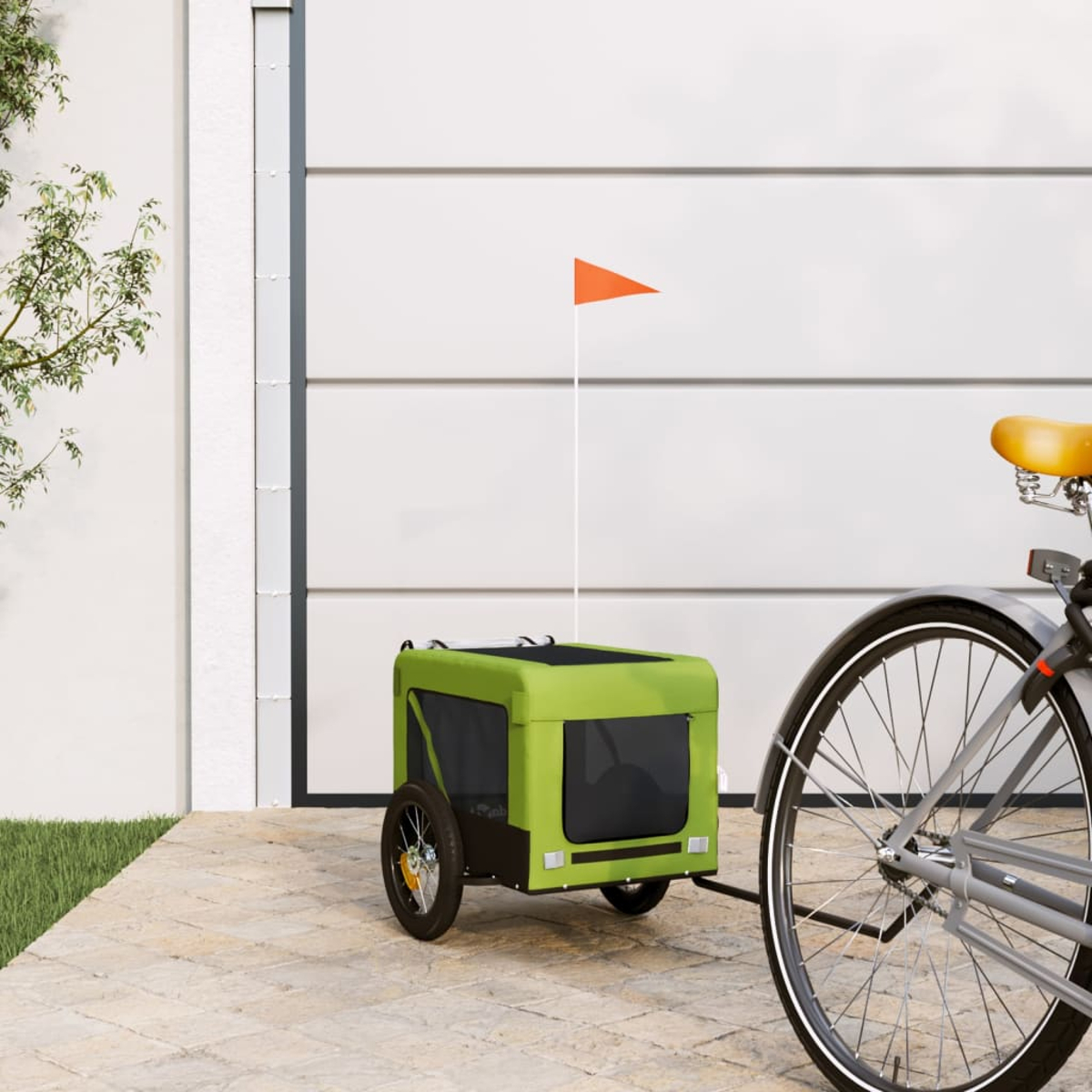 Ein Fahrrad mit gelbem Sattel zieht einen grünen Tieranhänger mit einer orangefarbenen Flagge. Im Hintergrund ist ein weißes Garagentor zu sehen.