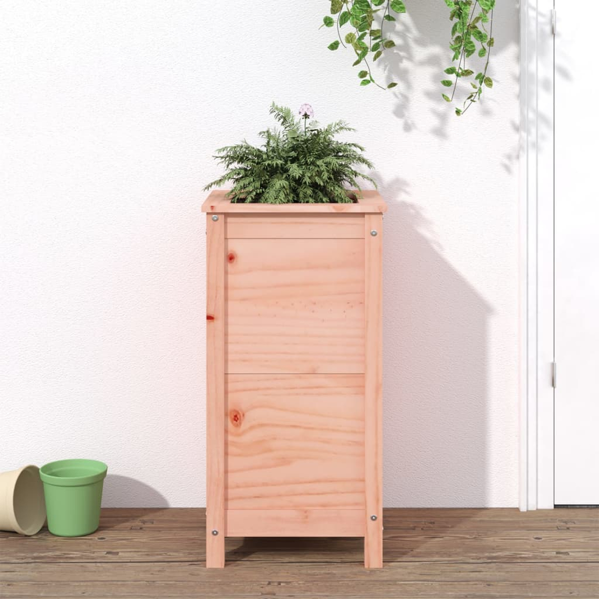 Eine Holzpflanzkasten mit einer grünen Pflanze. Ein grüner und ein beiger Topf stehen auf dem Boden. Weiße Wand und Tür im Hintergrund.