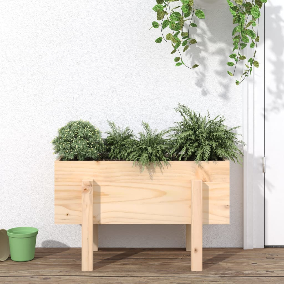Ein hölzerner Pflanzkasten mit grünen Pflanzen steht auf einem Holzdeck. Ein grüner Topf und eine Ranke hängen von oben.