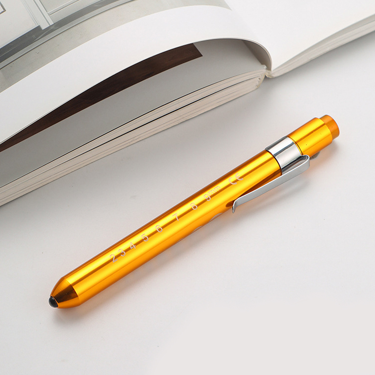 Ein goldfarbener Stift liegt auf einer weißen Oberfläche neben einem offenen Buch.