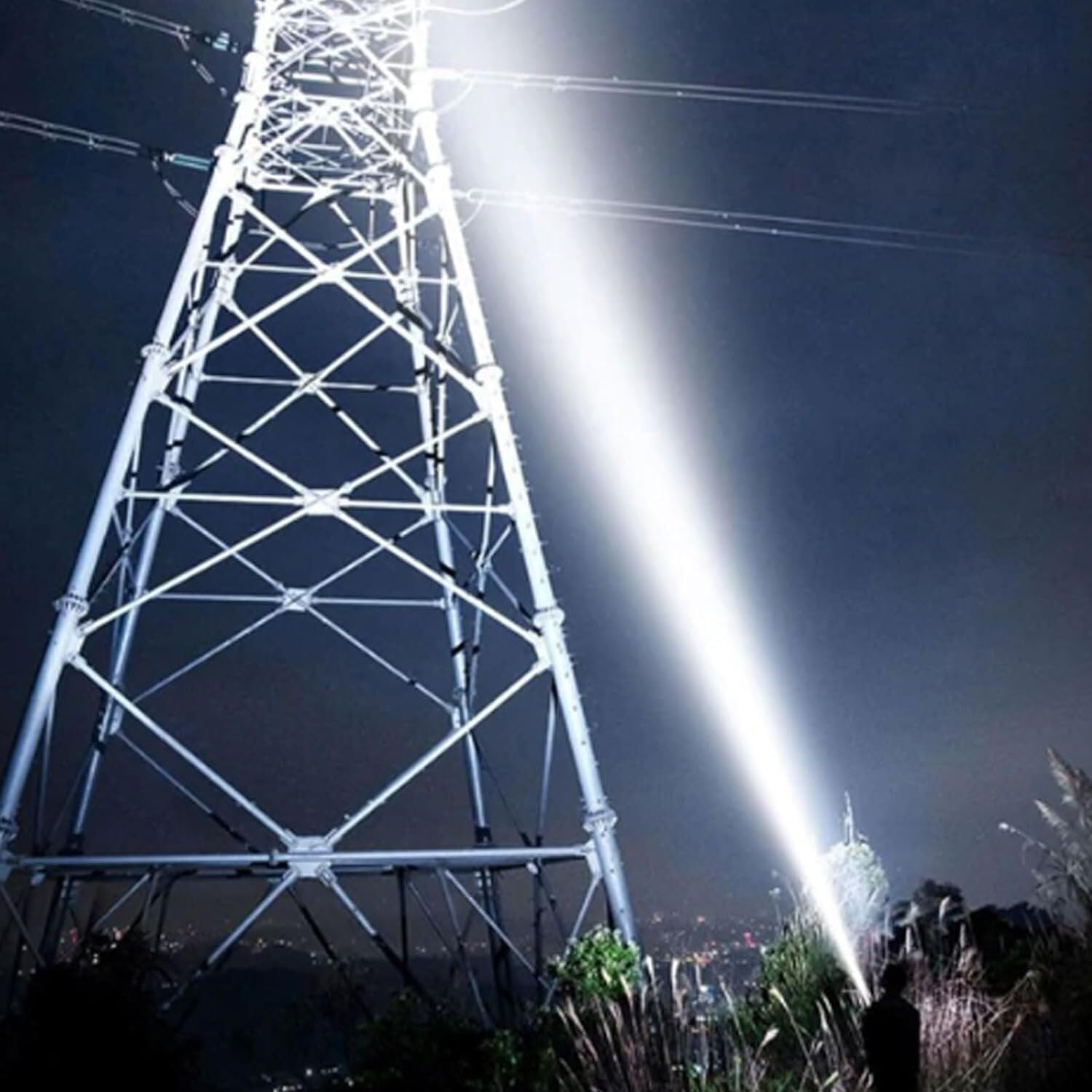 Eine Person leuchtet nachts mit hellem Licht auf einen Strommast. Der Himmel ist dunkel, und der Pylon hat viele Leitungen.