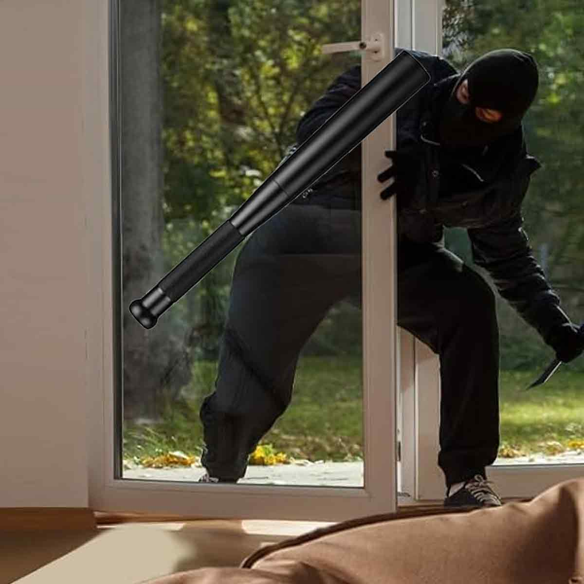 Eine Person in schwarzer Kleidung und Sturmhaube bricht mit einem Schlagstock und einem Messer in ein Haus ein. Bäume sind draußen sichtbar.
