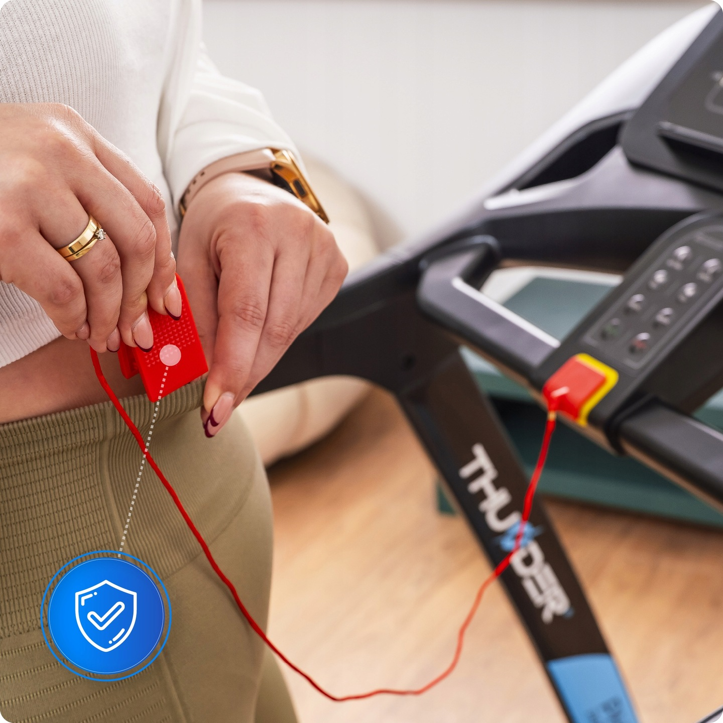 Osoba trzyma czerwoną kluczyk bezpieczeństwa przymocowany do bieżni. Osoba ma na sobie białą koszulę i złoty pierścionek.