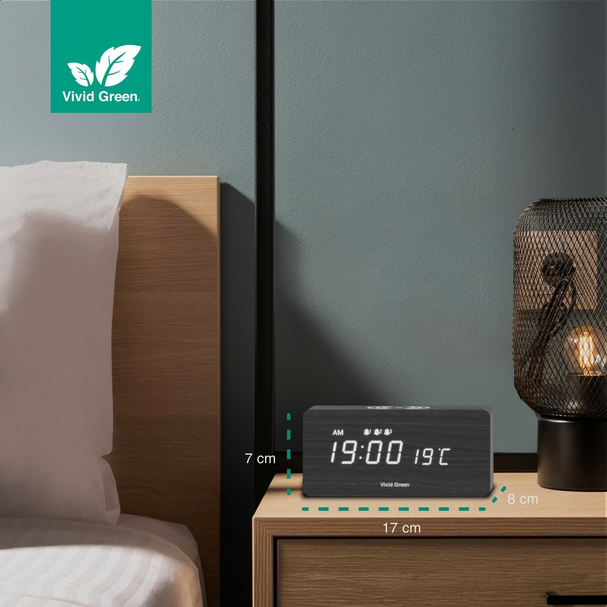 A wooden bedside table with a digital clock displaying time and temperature. A lamp and part of a bed are also visible.