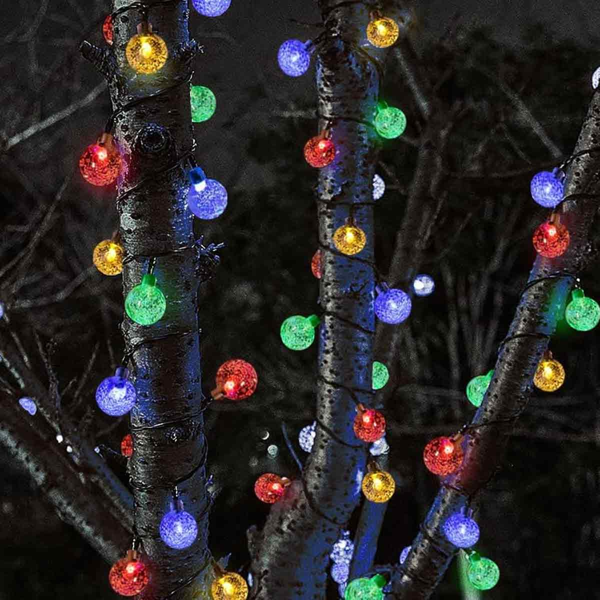 Lichterketten mit bunten Glühbirnen, die um Äste gewickelt sind. Rote, grüne, gelbe und blaue Lichter leuchten vor dunklem Hintergrund.
