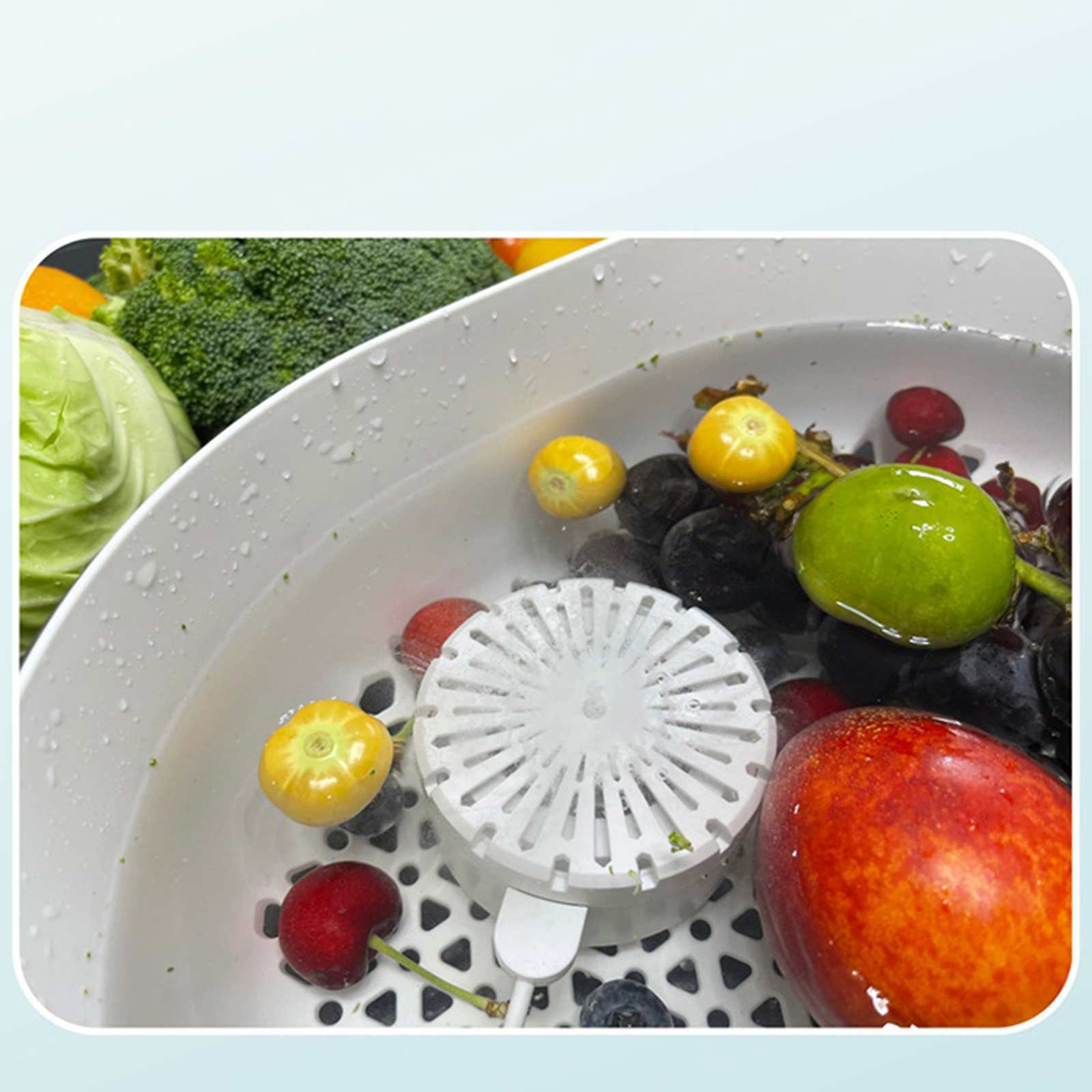 Ein weißes Becken enthält Früchte wie Trauben, Kirschen und einen Pfirsich. Brokkoli und Kohl liegen daneben.