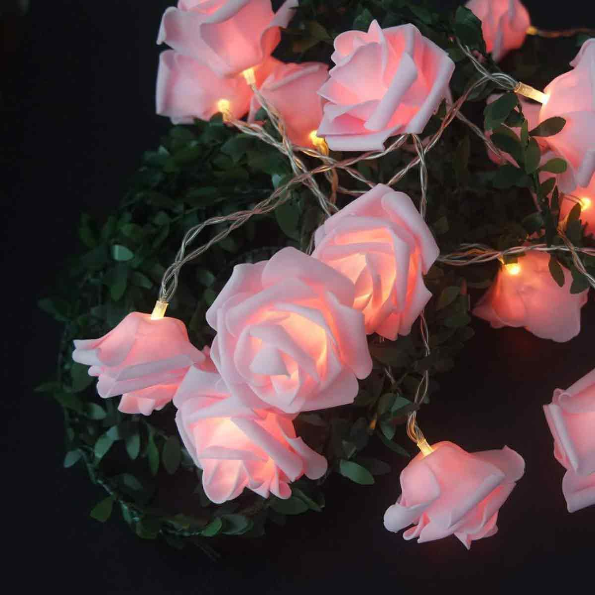 Rosa Rosen-Lichterkette auf grünem, belaubtem Hintergrund mit dunklem Hintergrund. Die Rosen leuchten sanft.