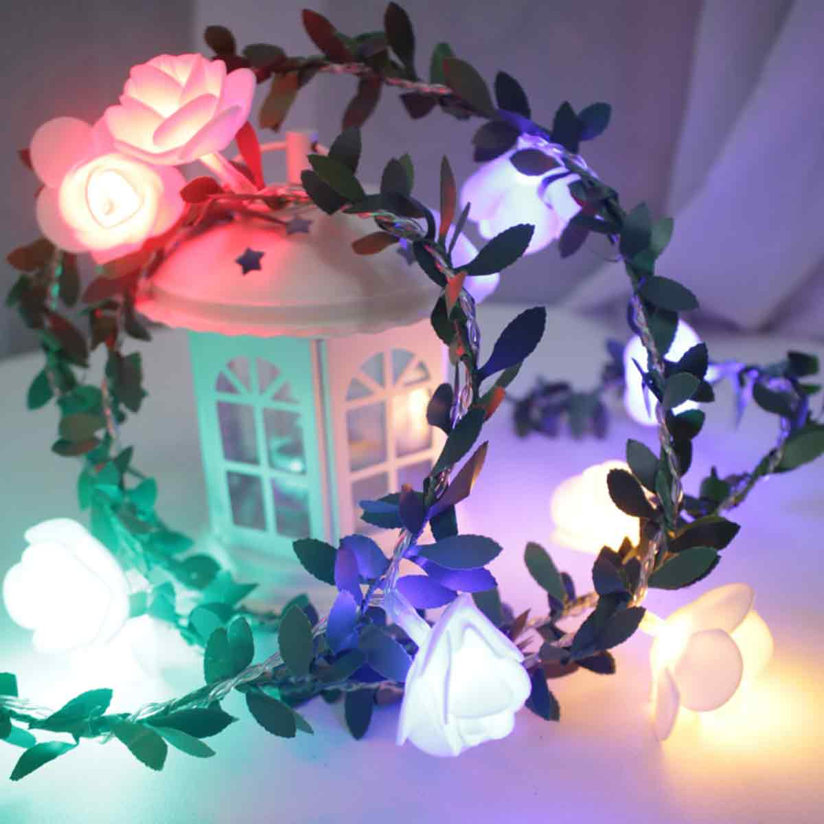 Eine weiße Laterne mit einem Kranz aus Lichtern und Blättern. Die Lichter sind rosenförmig und leuchten in verschiedenen Farben.