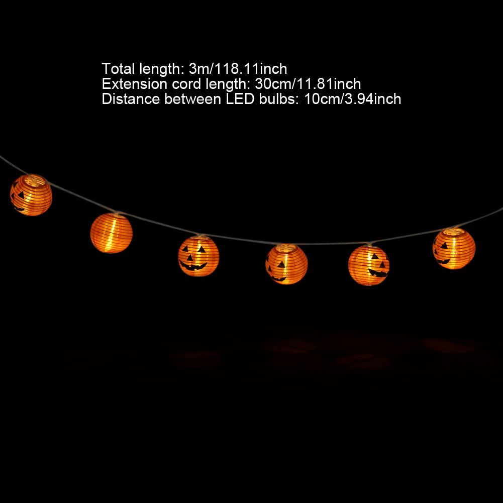 Eine Schnur mit orangefarbenen, kürbisförmigen Lichtern hängt vor einem schwarzen Hintergrund. Jedes Licht hat ein geschnitztes Gesicht.