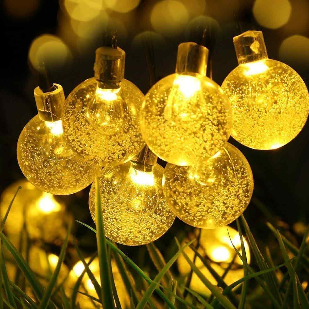 Nahaufnahme von leuchtenden, runden, gelben Lichterketten auf Gras. Einige Lichter sind scharf, andere im Hintergrund unscharf. Abendszene.