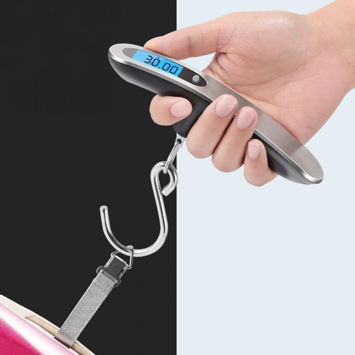 Eine Hand hält eine digitale Gepäckwaage mit der Anzeige 30,00. Ein Metallhaken ist an einem Kofferriemen befestigt, vor schwarz-weißem Hintergrund.