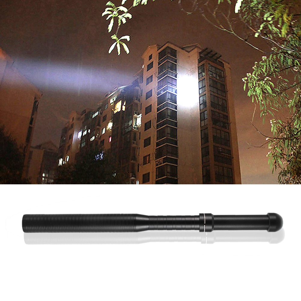 Eine schwarze Taschenlampe vor einem Gebäude, das nachts von einem Lichtstrahl beleuchtet wird. Bäume sind im Hintergrund zu sehen.
